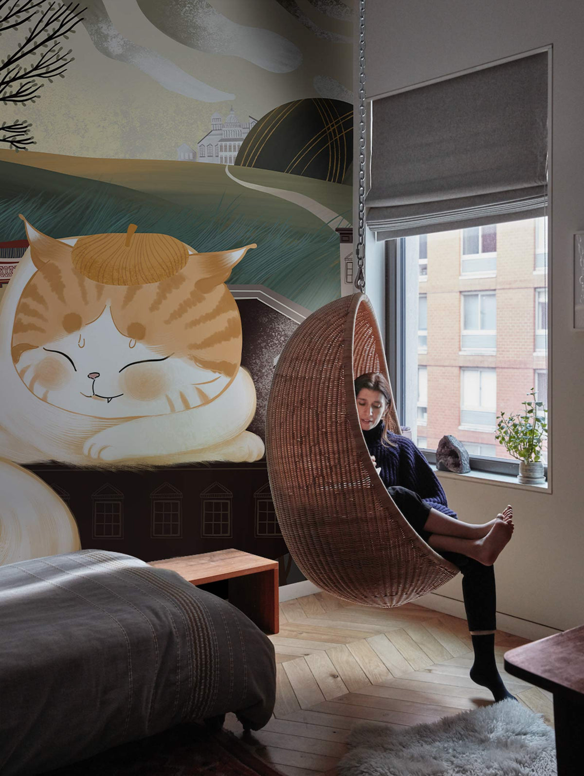 Charming Whimsical Cat Mural Wallpaper adorns bedroom with chevron wood flooring and wicker hanging chair.