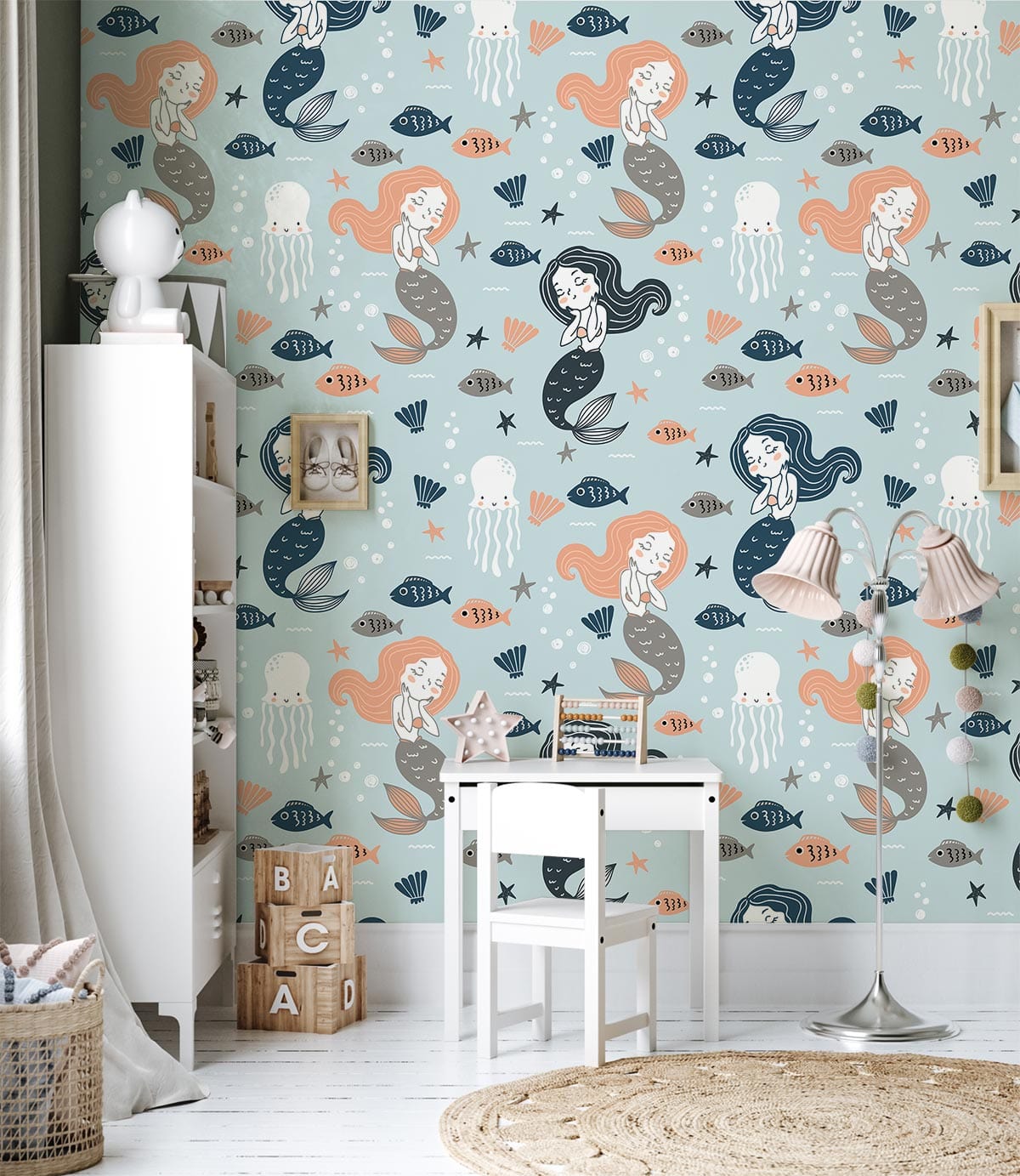 Children's room with whimsical mermaid wallpaper, pastel blue and coral tones, white furniture, woven rug.