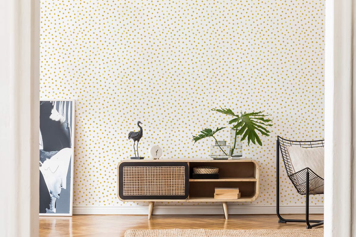 Golden Polka Dot Wallpaper in modern living room with rattan console, chic chair, wooden flooring.