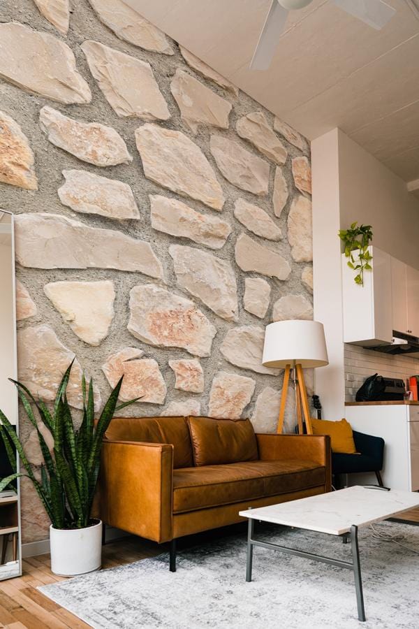 Beige and grey stone wallpaper, brown leather sofa, white lamp, in modern living room interior.