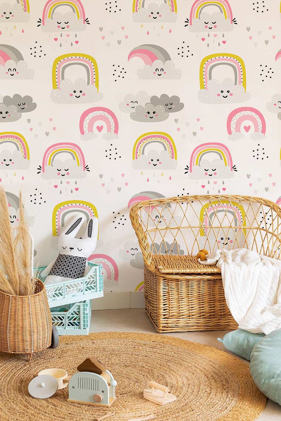Whimsical nursery wallpaper mural with pink and grey clouds, rainbow patterns, rattan chair, wicker basket.