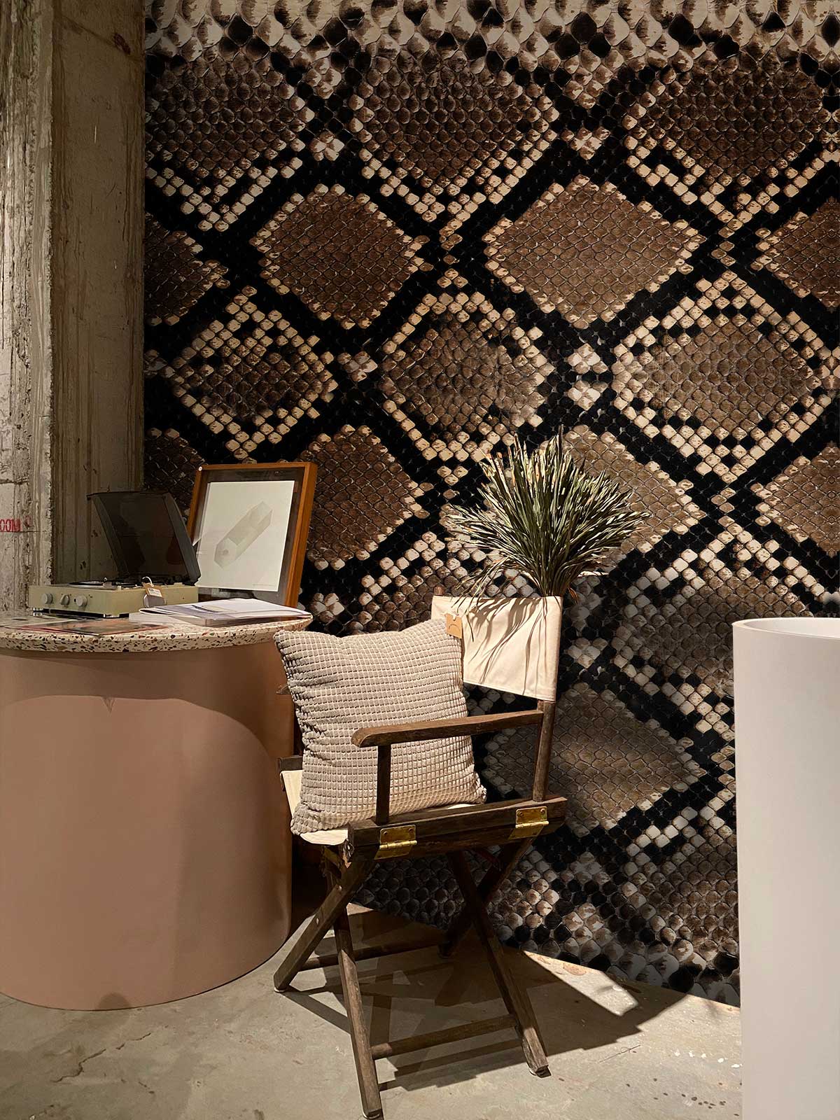 Exotic brown snake skin pattern wallpaper, wooden chair, cushioned pillow, cylindrical side table, stylish interior.
