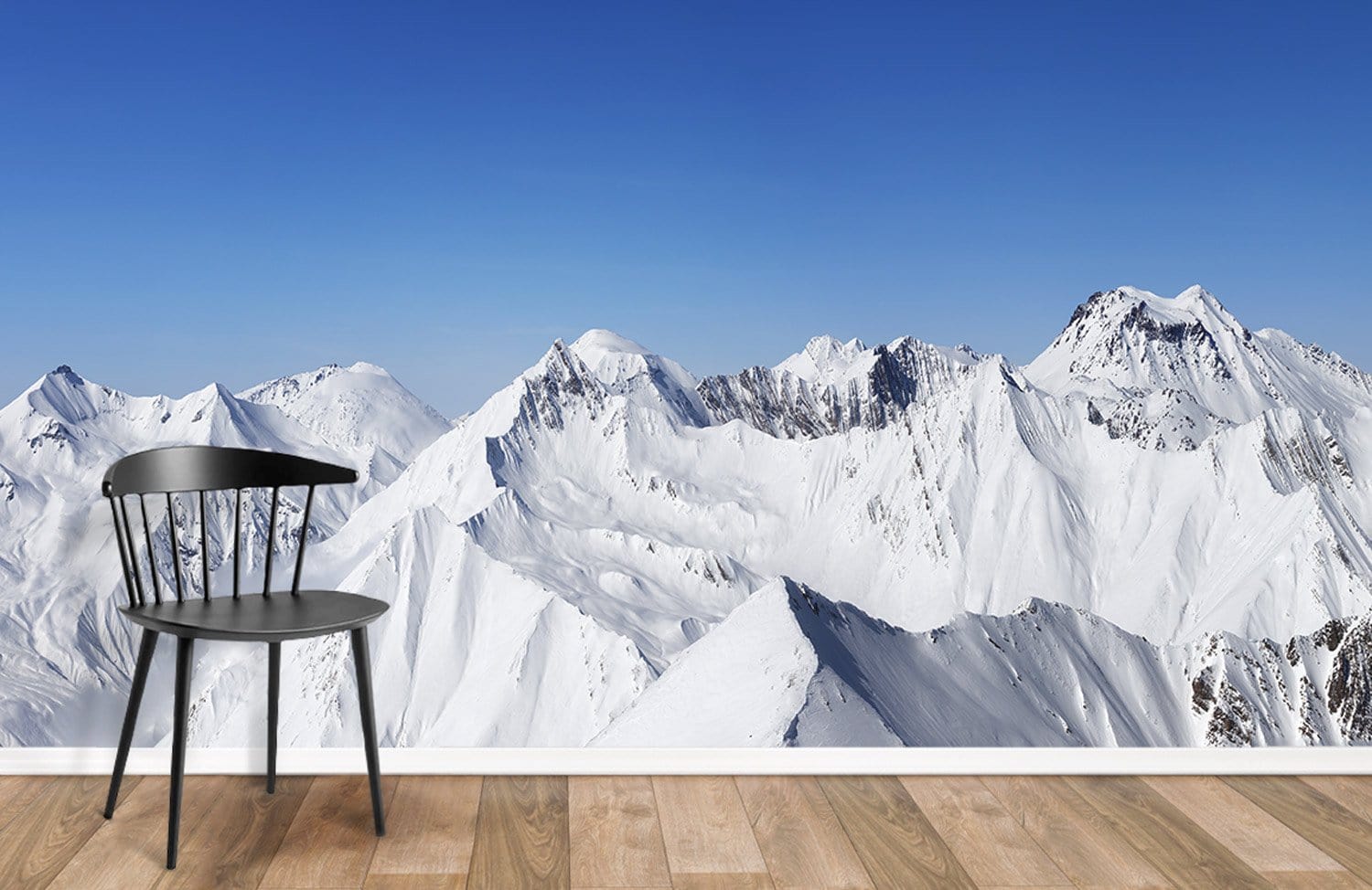 Snowy mountain mural wallpaper in room with wooden flooring and modern black chair.