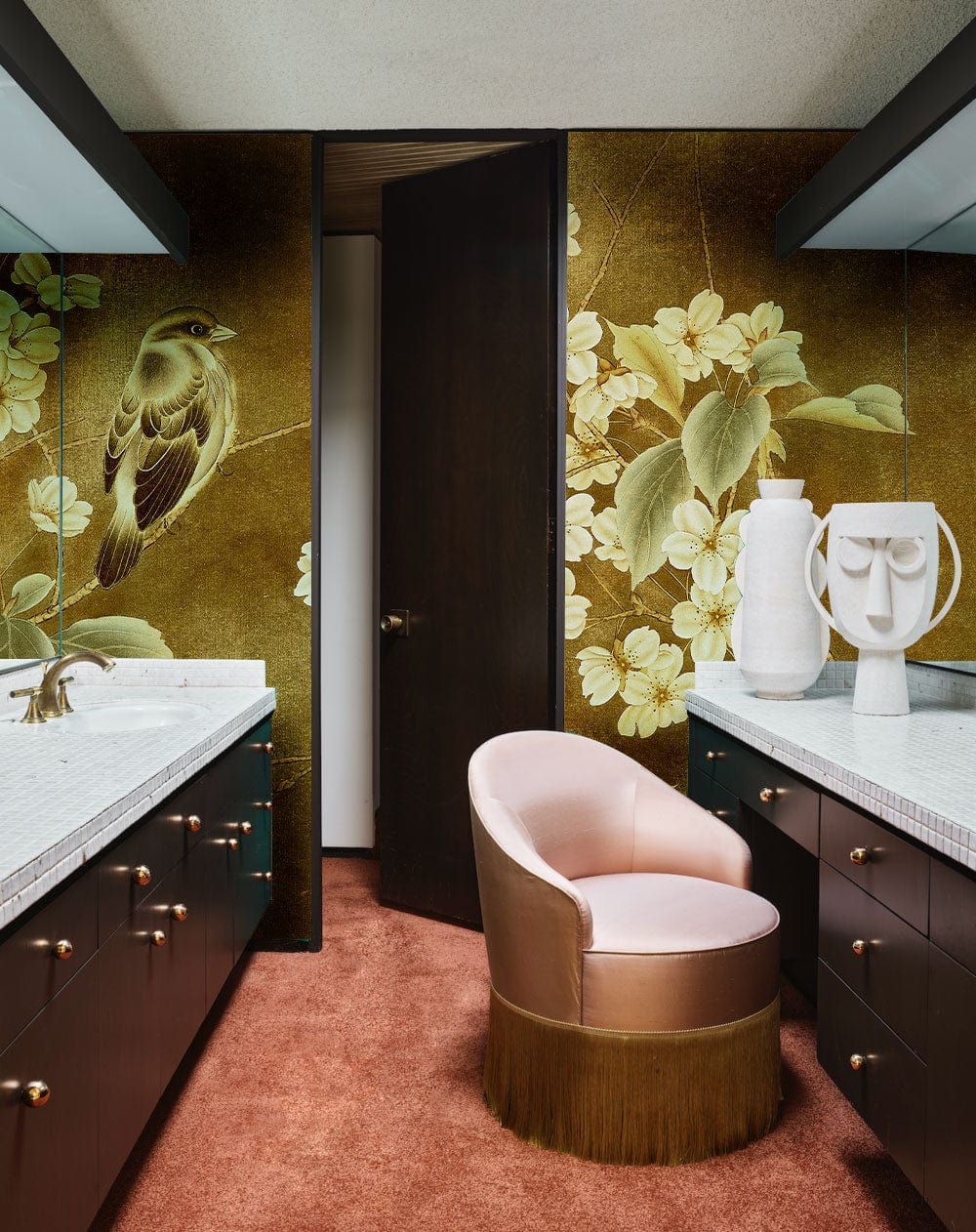 Vintage floral bird mural wallpaper in golden tones, pink armchair, brown cabinets, plush carpet, bathroom.