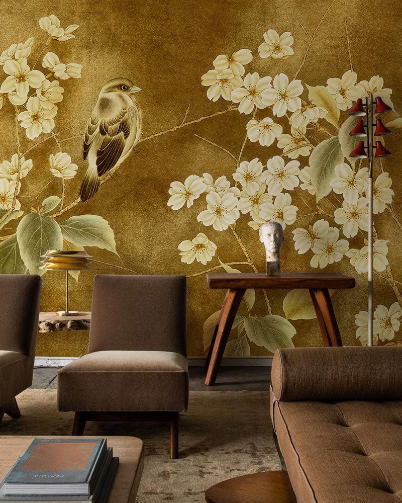 Vintage floral bird mural wallpaper in golden tones with brown sofa, modern chairs, living room setting.