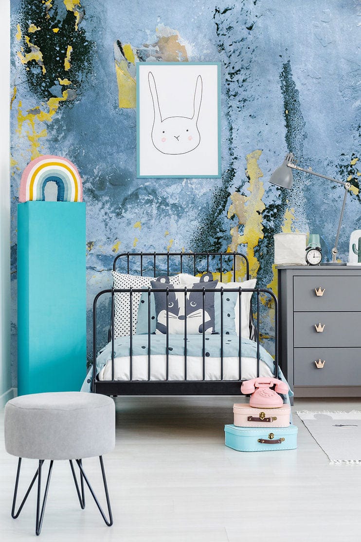 Contemporary children's room with abstract blue and gold textured mural wallpaper, grey dresser, and black bed.