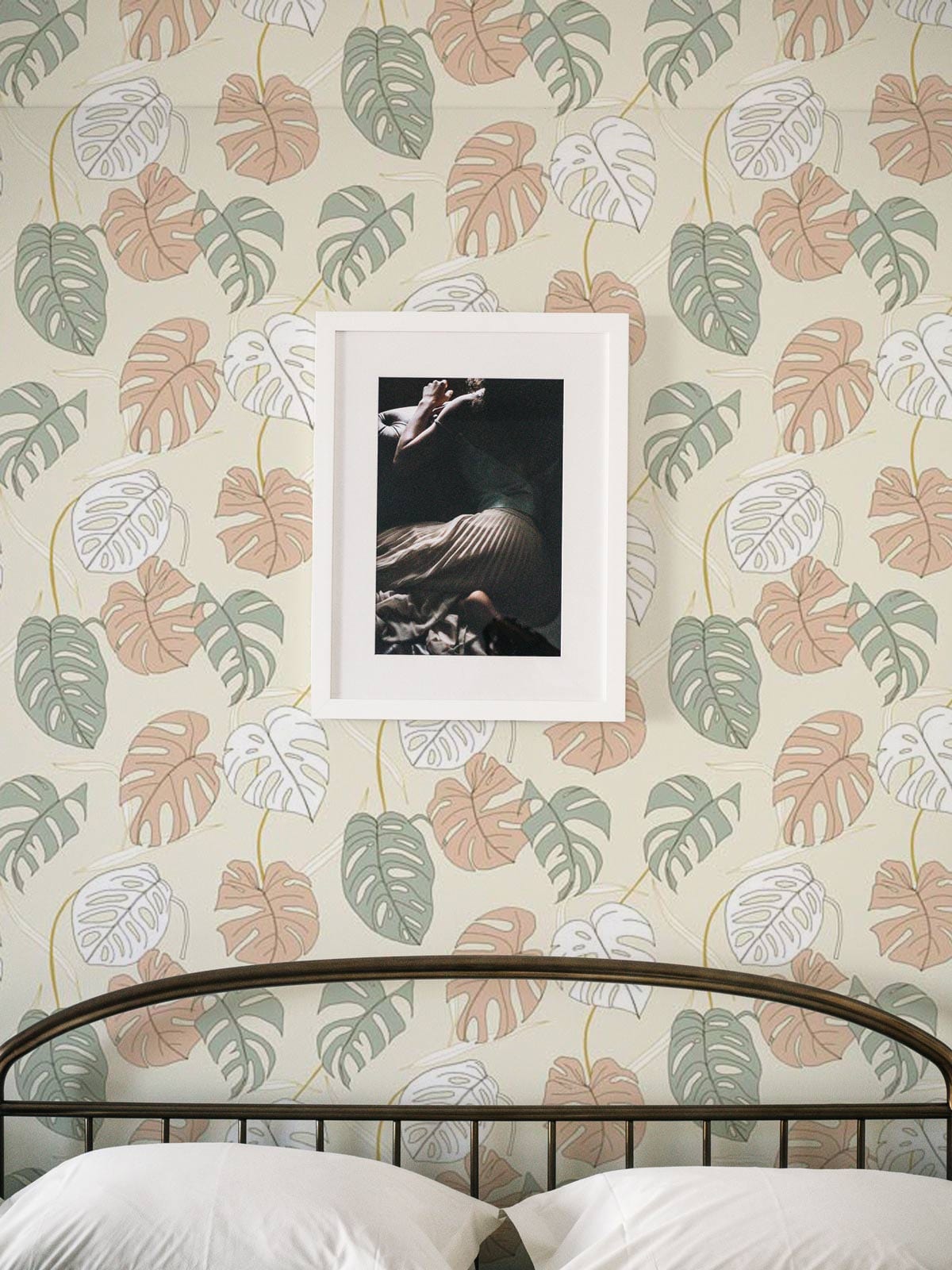 Pastel green and peach tropical leaf wallpaper with framed art above black metal bed in bedroom.