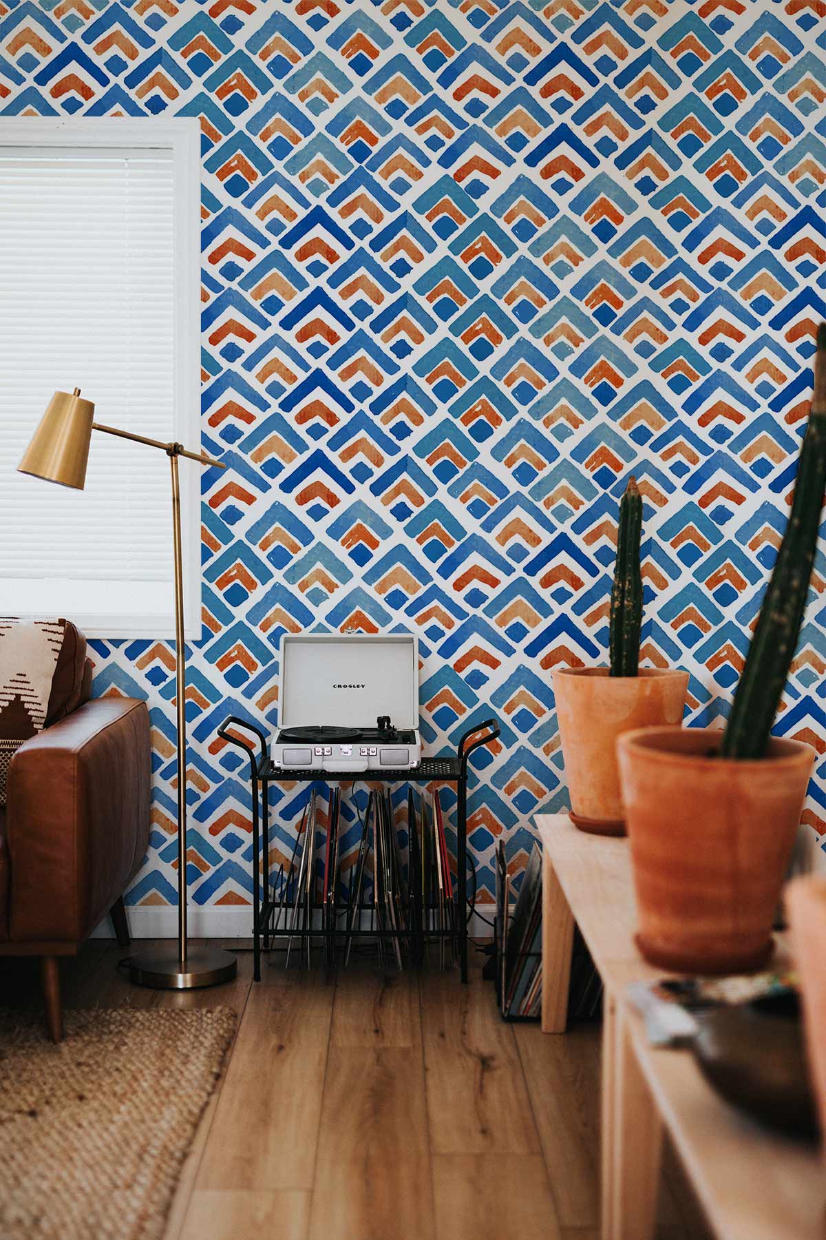 Blue and orange geometric wallpaper, modern lampshade, wooden flooring, brown sofa, contemporary living room.