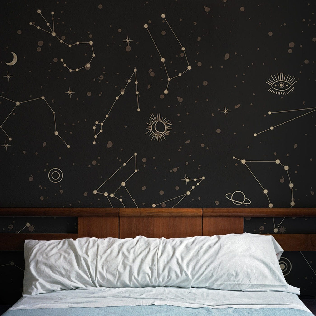Cosmic Constellations black starry night wallpaper mural behind bed, wooden headboard, cosy bedroom setting.