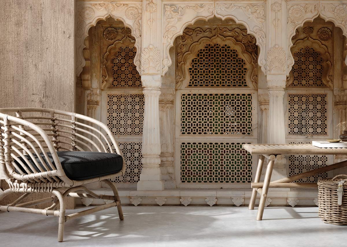 Elegant wallpaper with Indian arch design, rattan chair, wooden table, in a modern living room.