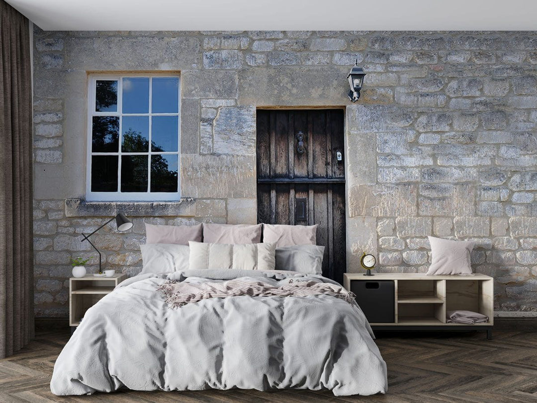 Rustic stone cottage wall mural with wooden door, bedroom, grey bedding, wooden flooring, elegant lamp.