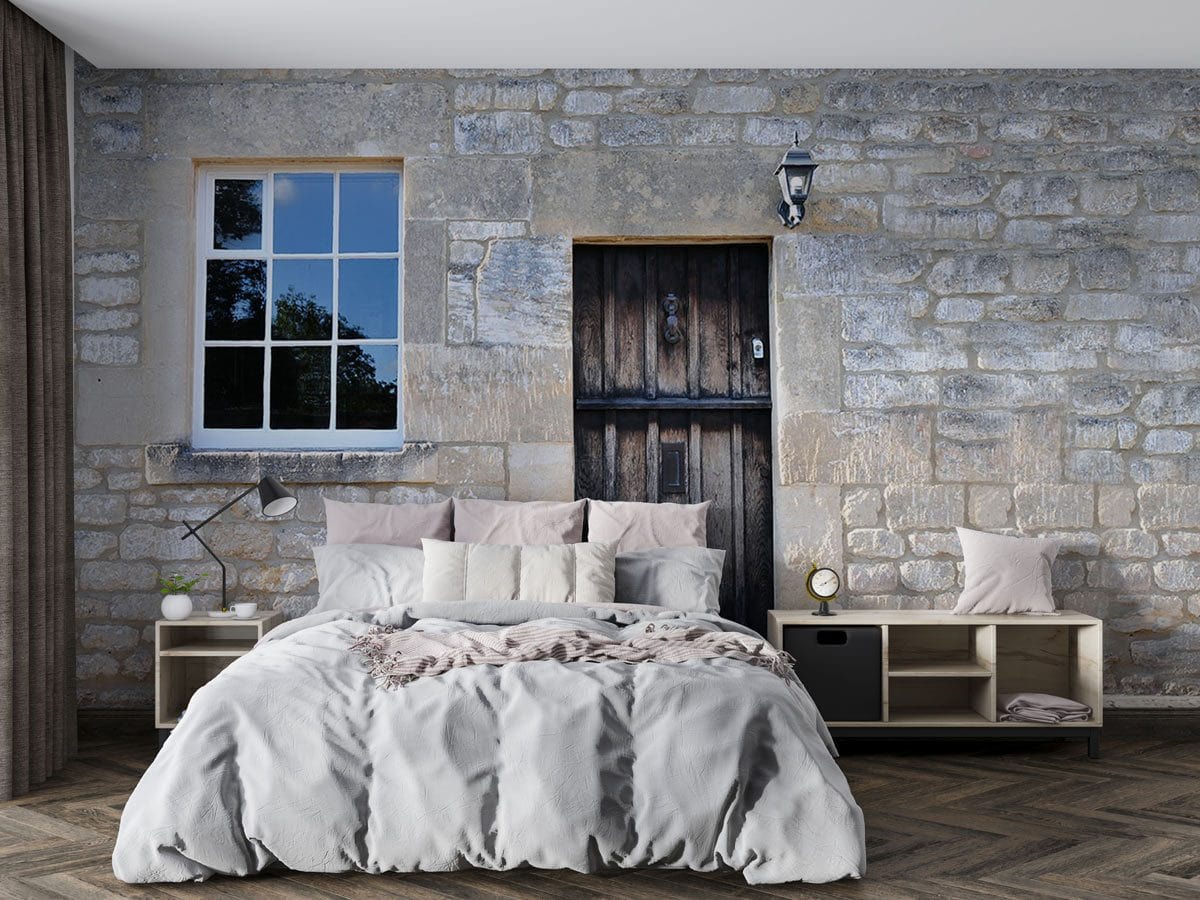 Rustic stone cottage wall mural with wooden door, bedroom, grey bedding, wooden flooring, elegant lamp.