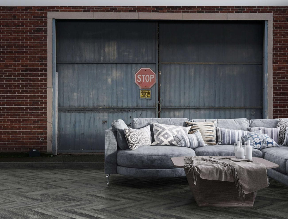 Industrial grey mural wallpaper with stop sign, grey sectional sofa, chevron flooring, urban decor.
