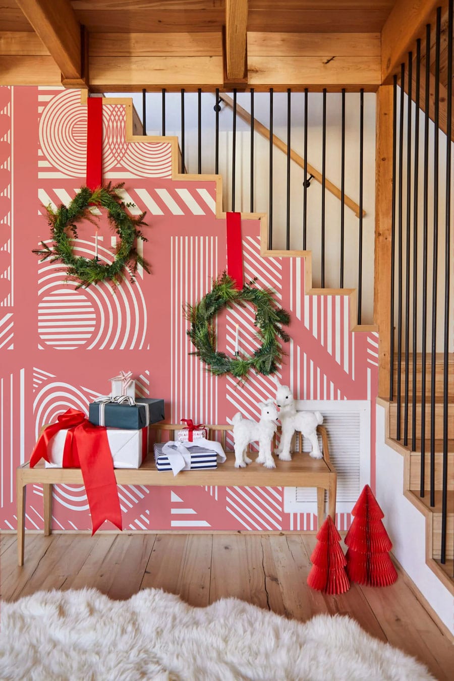 Geometric coral pink retro mural wallpaper; wooden stairs; fur rug; festive wreaths; modern hallway.