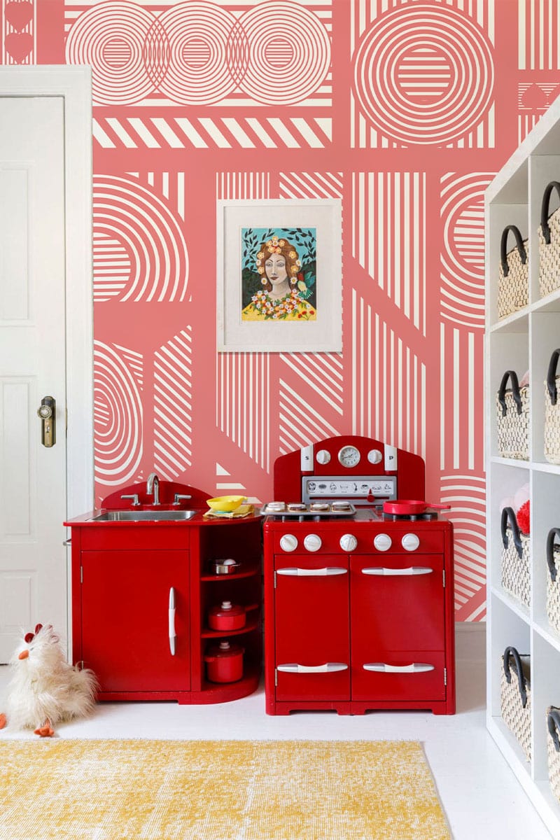 Geometric coral pink retro wallpaper, red play kitchen, white shelving, nursery room, yellow rug.
