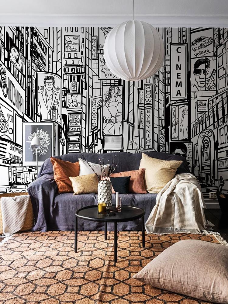 Monochrome urban cityscape mural with grey sofa, patterned rug, modern pendant light, graphic street scene.