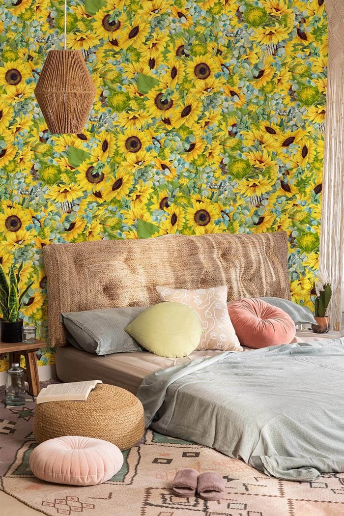 Sunflower wallpaper with wicker headboard, green bedspread, pink cushions, woven pendant in bedroom setting.