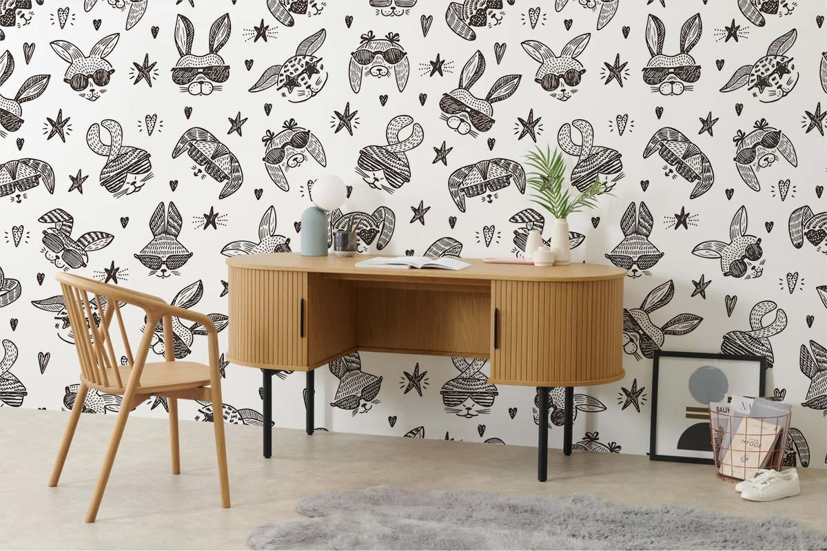 Kids' playroom with whimsical bunny wallpaper, wooden desk, chair, grey rug, and minimalistic decor accents.