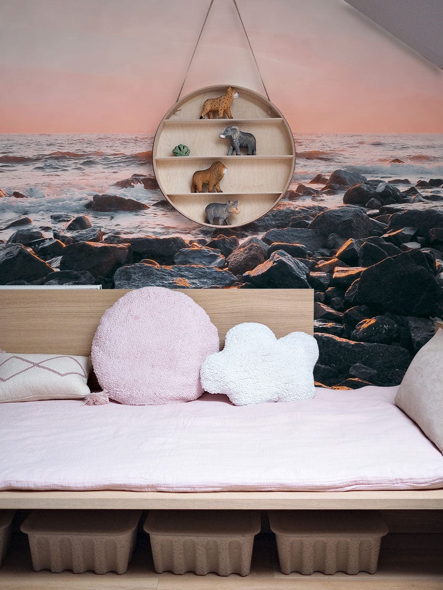 Serene Coastal Sunrise Mural Wallpaper in pink and blue, wooden bed, pastel decor, circular shelf, nursery.