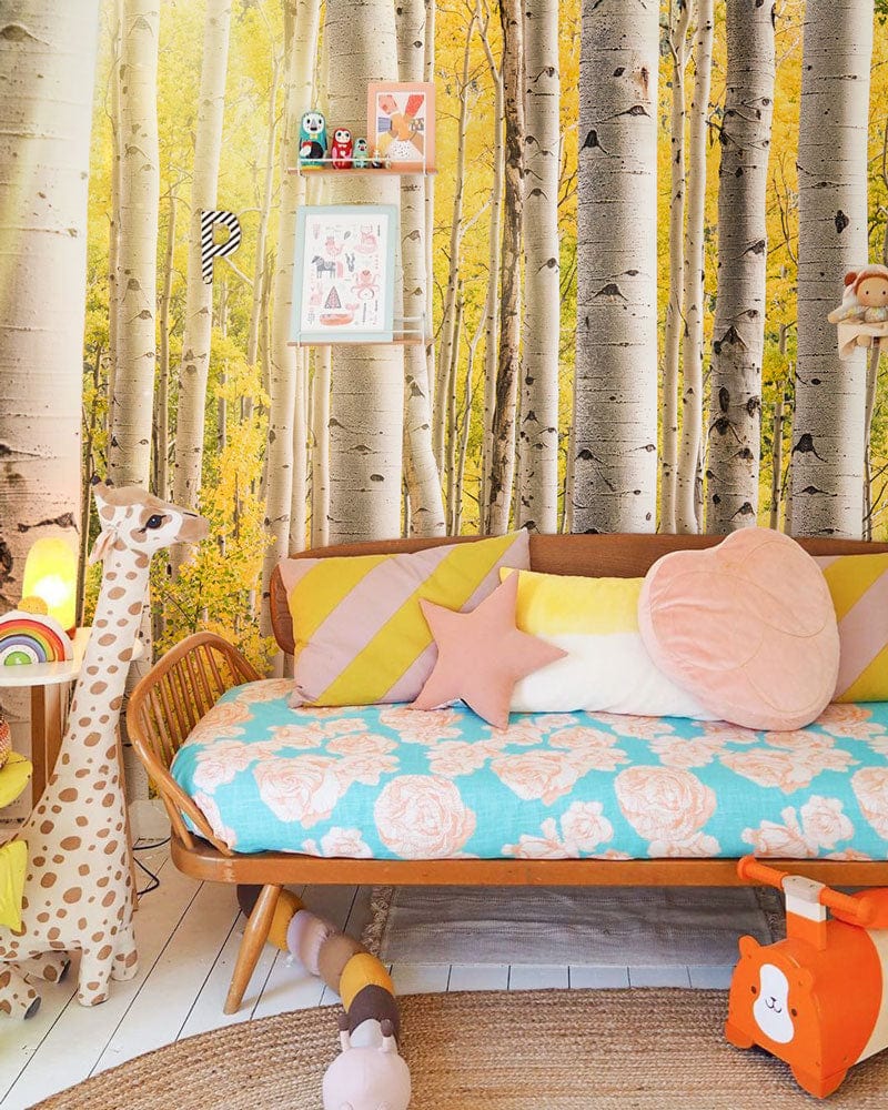 Golden Autumn Birch Forest Mural Wallpaper in children's room with wooden sofa, giraffe toy, playful decor.