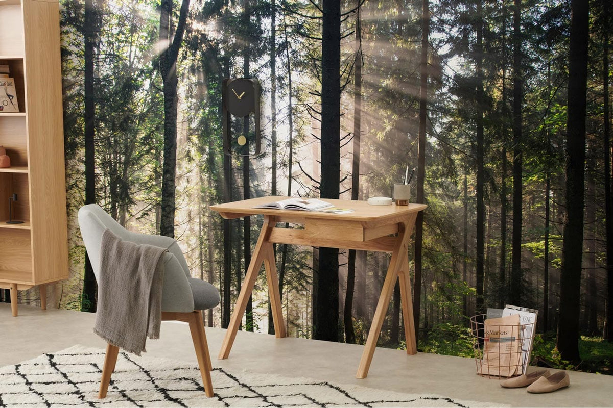 Mystical Forest Sunrise wallpaper, grey chair, light wood desk, rug, and clock in modern study.