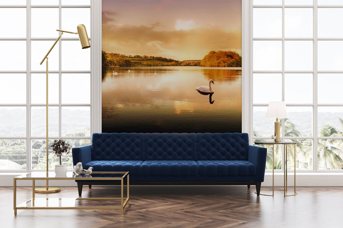 Golden Sunset Lake Scene Mural Wallpaper with serene swan, blue sofa, gold lamp, parquet flooring.