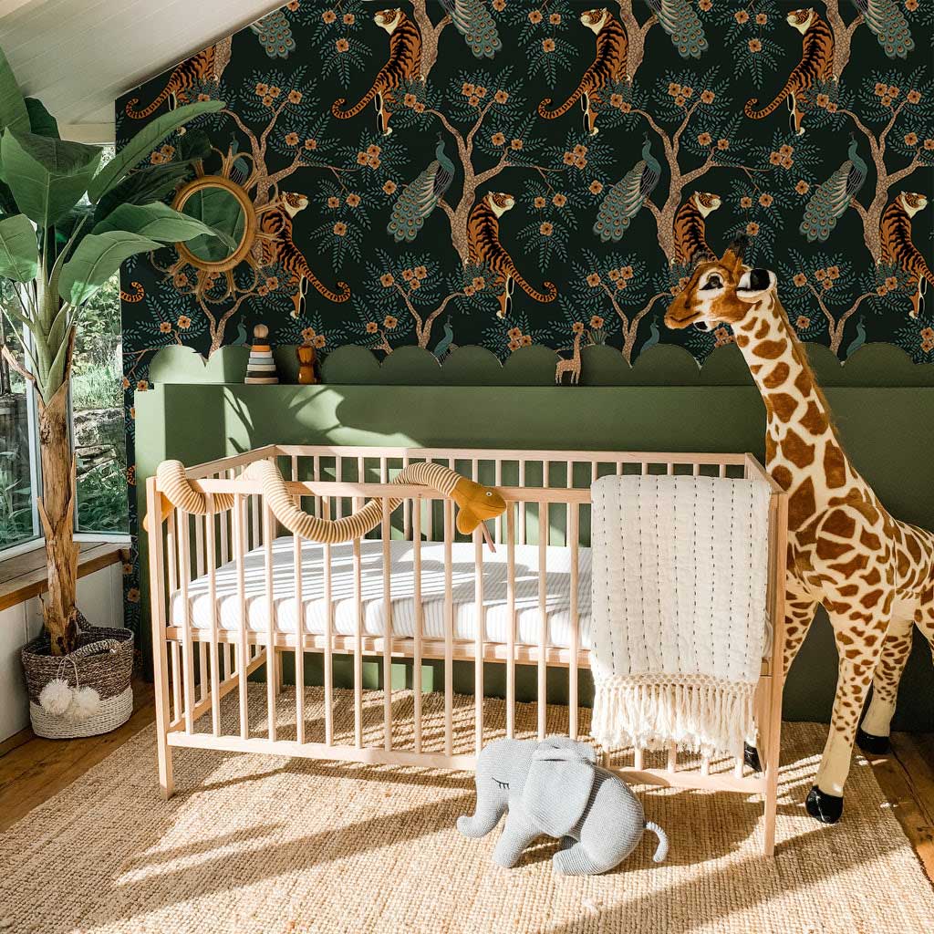 Elegant dark green jungle wallpaper in nursery; wooden cot, giraffe decor, natural fibre flooring.