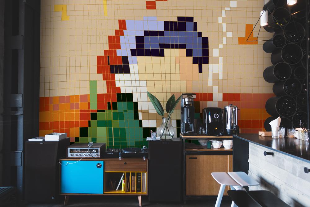 Vibrant multicolour mosaic wallpaper in contemporary room with black shelving, light wood cabinets, and vinyl player.