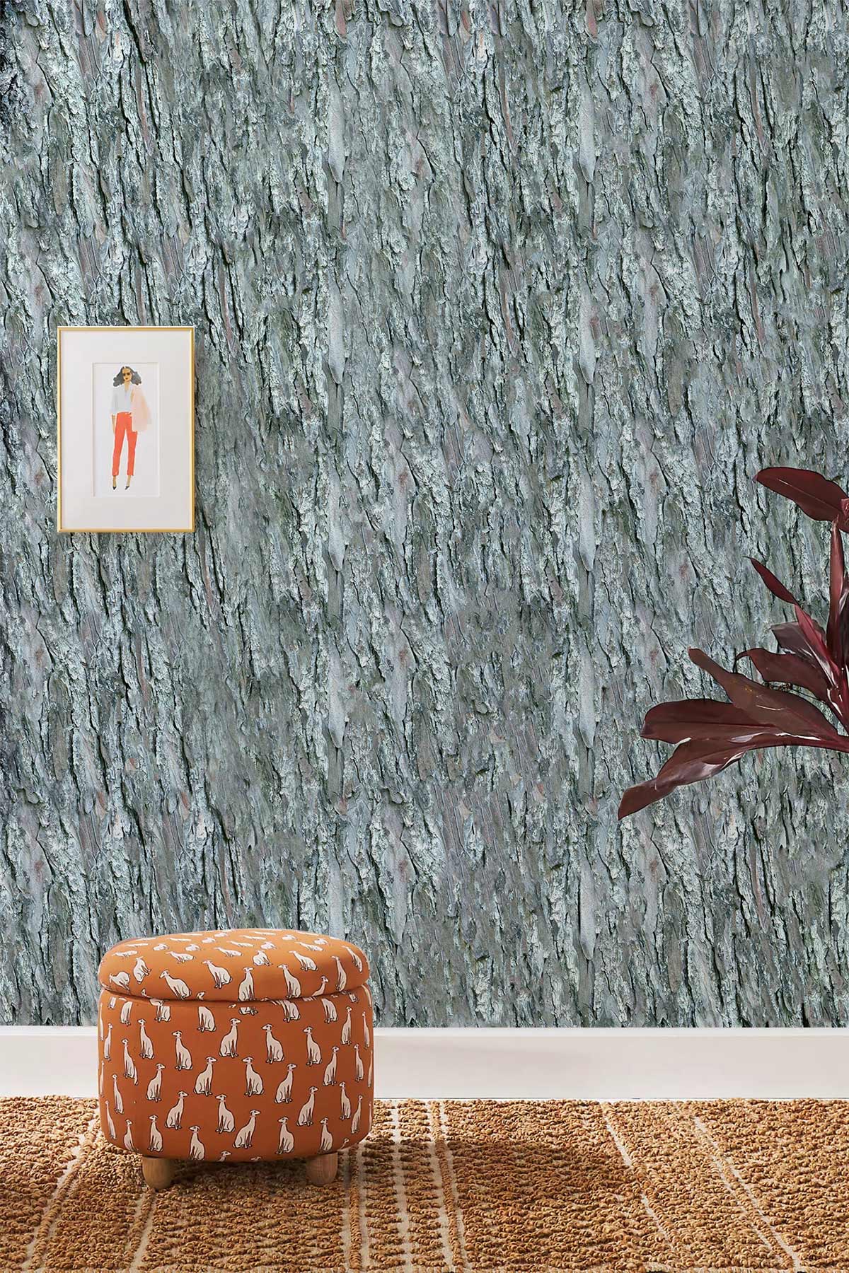 Elegant grey tree bark wallpaper, orange patterned ottoman, framed art, rug, plant decor in living room.