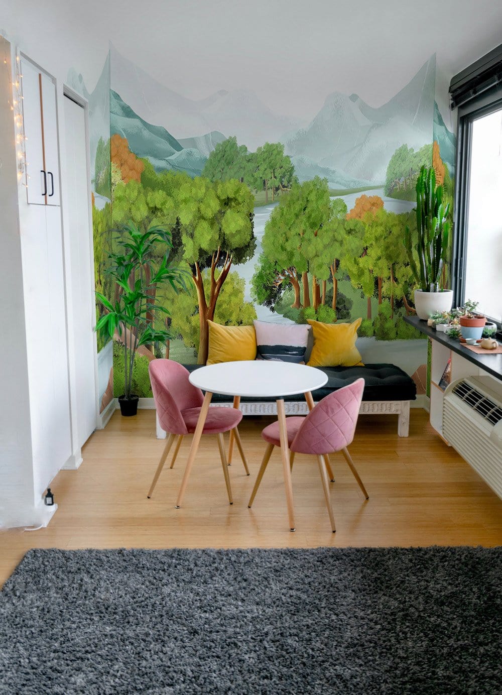 Tranquil green forest landscape mural wallpaper in living room with pink chairs, wooden flooring.