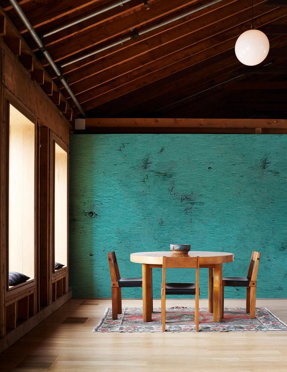 Vintage teal distressed wallpaper in rustic dining room, wooden ceiling, oak flooring, round table.