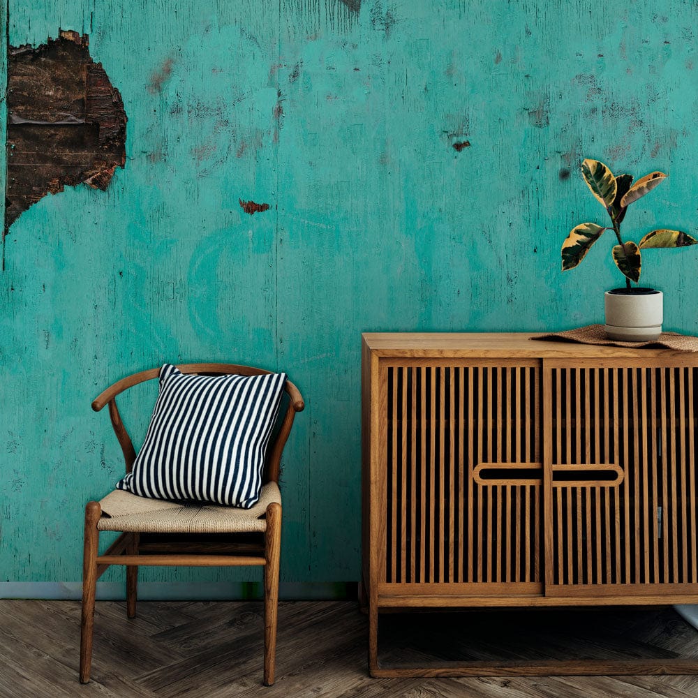 Rustic turquoise wallpaper complementing vintage furniture, wooden chair, striped cushion, and distressed industrial charm.