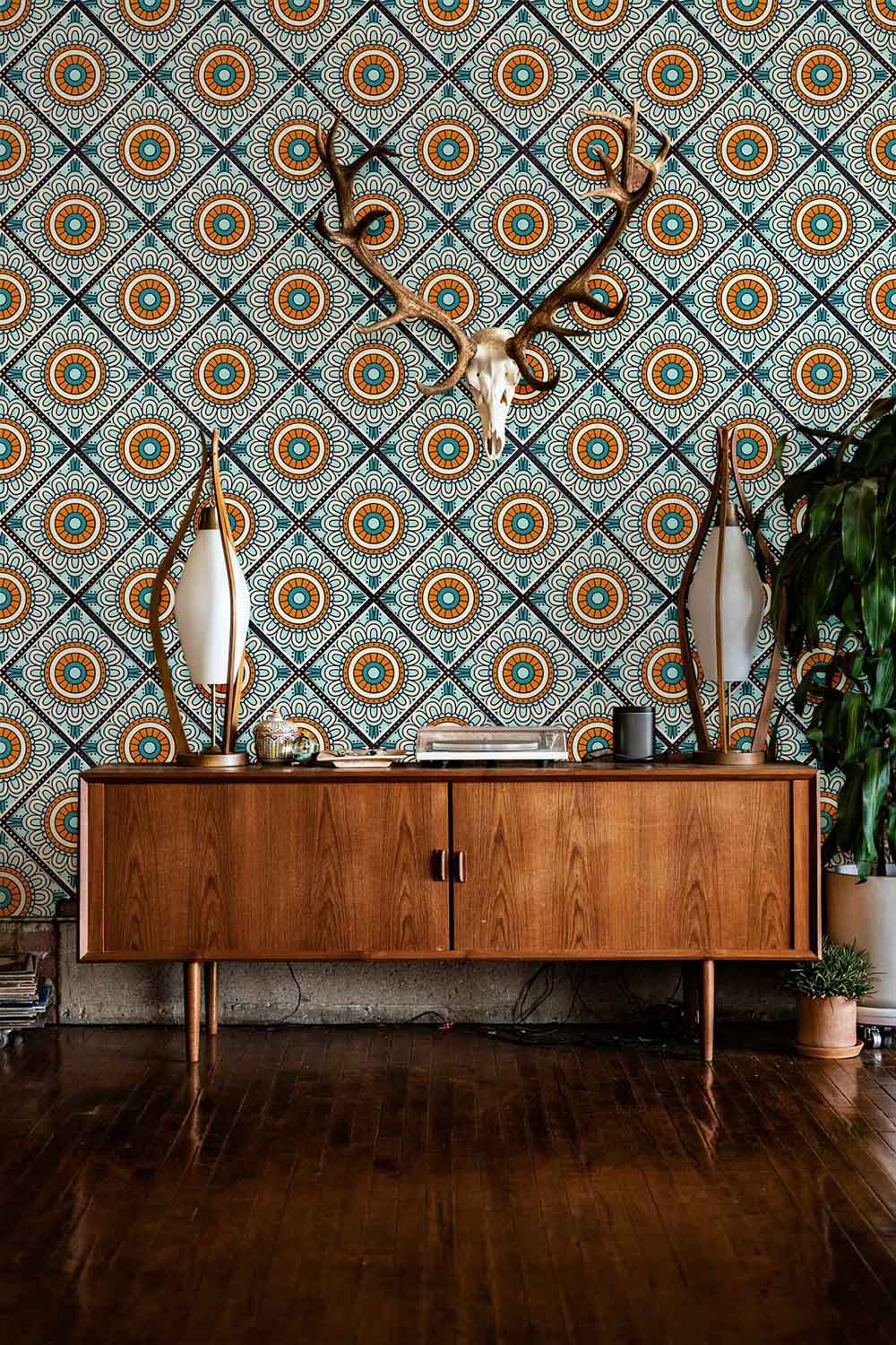 Vintage teal and orange floral geometric wallpaper, wooden sideboard, antler decor, chic interior design.