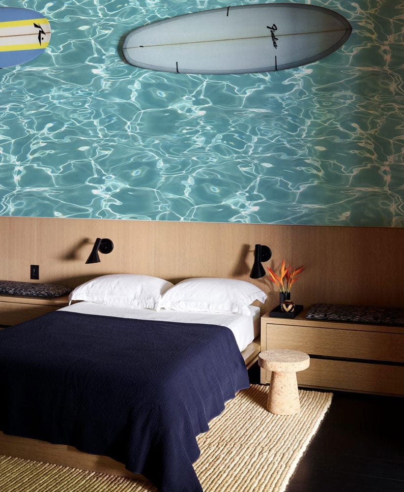 Tranquil Aqua Water Ripple Wallpaper in bedroom with wooden wall, navy bedding, and woven rug.