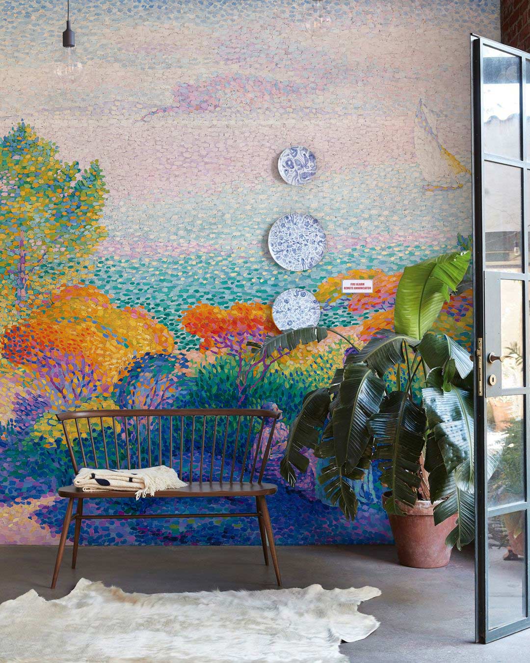Seaside Impressionist mural wallpaper with vibrant colours; wooden bench; concrete flooring; serene room setting.