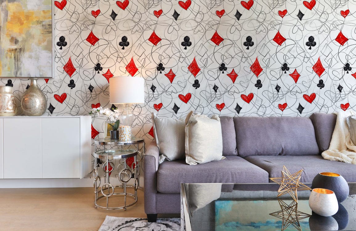 Patterned wallpaper with red and black playing cards in modern living room with grey sofa.