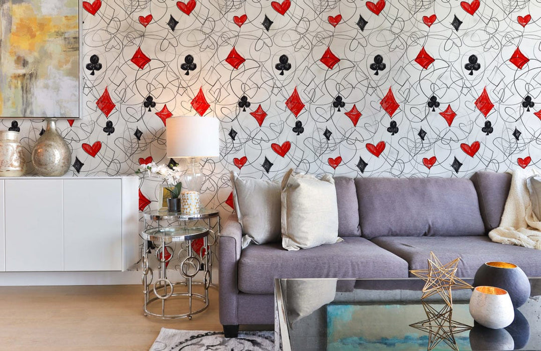 Patterned wallpaper with red and black playing cards in modern living room with grey sofa.