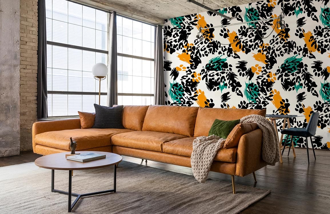 Bold Abstract wallpaper in black, orange, green behind brown leather sofa; industrial-style living room.