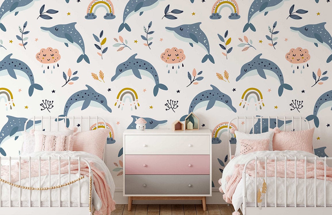 Playful blue dolphins nursery wallpaper featuring rainbows, clouds; white beds; pastel dresser; wooden flooring.