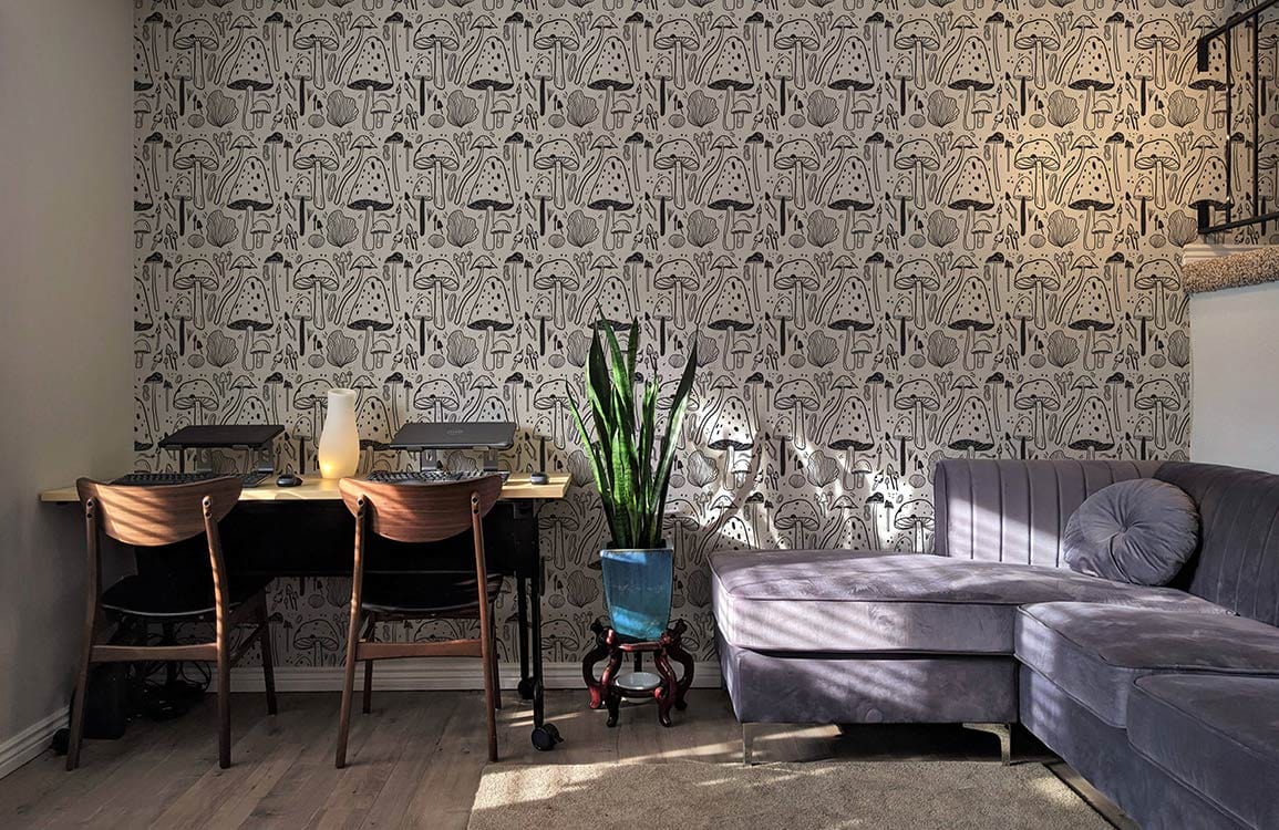 Alt text: Rustic Monochrome Mushroom Forest pattern wallpaper, grey sofa, wooden chairs, contemporary interior design.