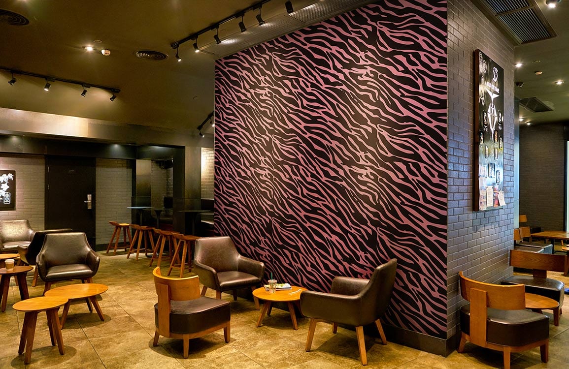 Pink and Black Zebra Wallpaper in cafe with black armchairs, wooden tables, and brick walls.