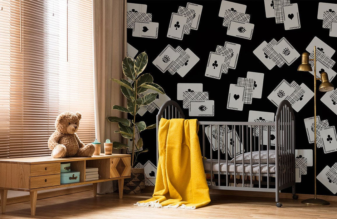 Monochrome playing cards wallpaper in nursery with yellow blanket, wooden flooring, and dark crib.