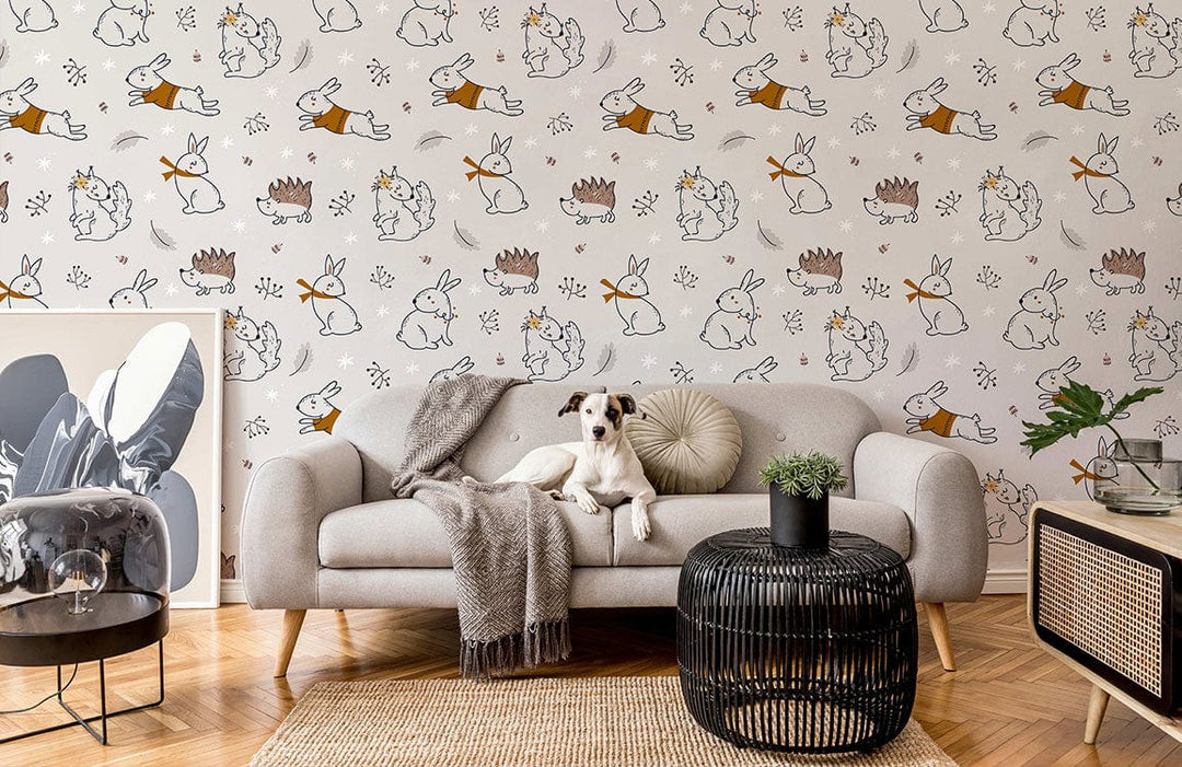 Whimsical nursery wallpaper with bunnies, hedgehogs; beige sofa, herringbone flooring, black wicker table, dog.