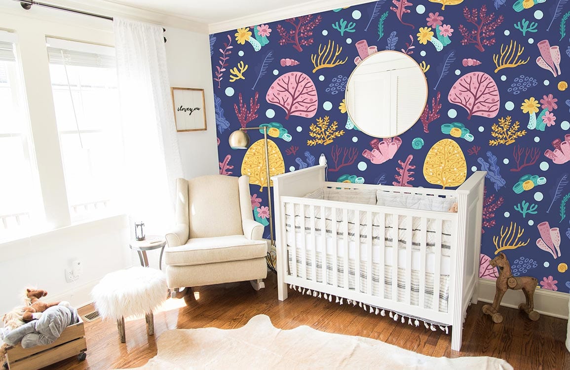 Navy blue sea life wallpaper in nursery with white crib, beige armchair, wooden floor, round mirror.