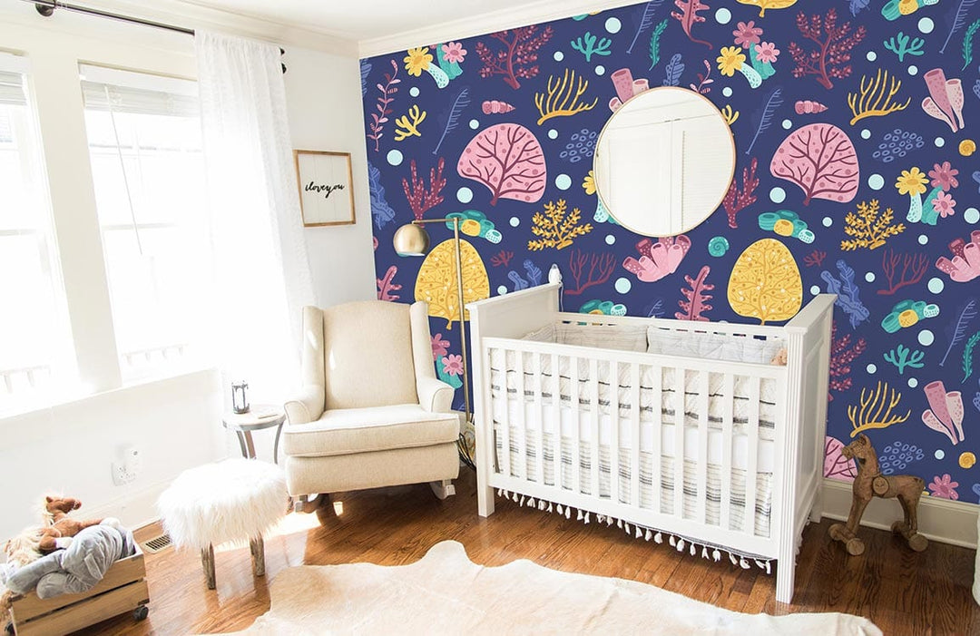 Navy blue sea life wallpaper in nursery with white crib, beige armchair, wooden floor, round mirror.