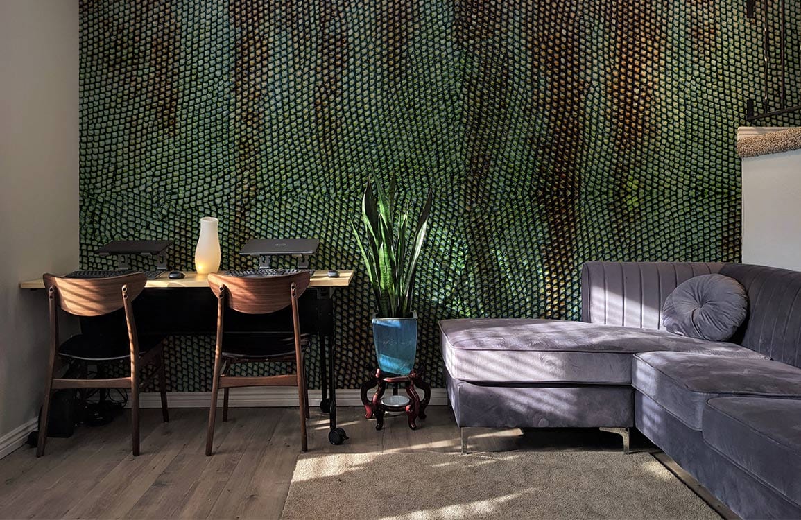 Rustic green wallpaper in living room with grey sectional sofa, wooden chairs, and light wood flooring.