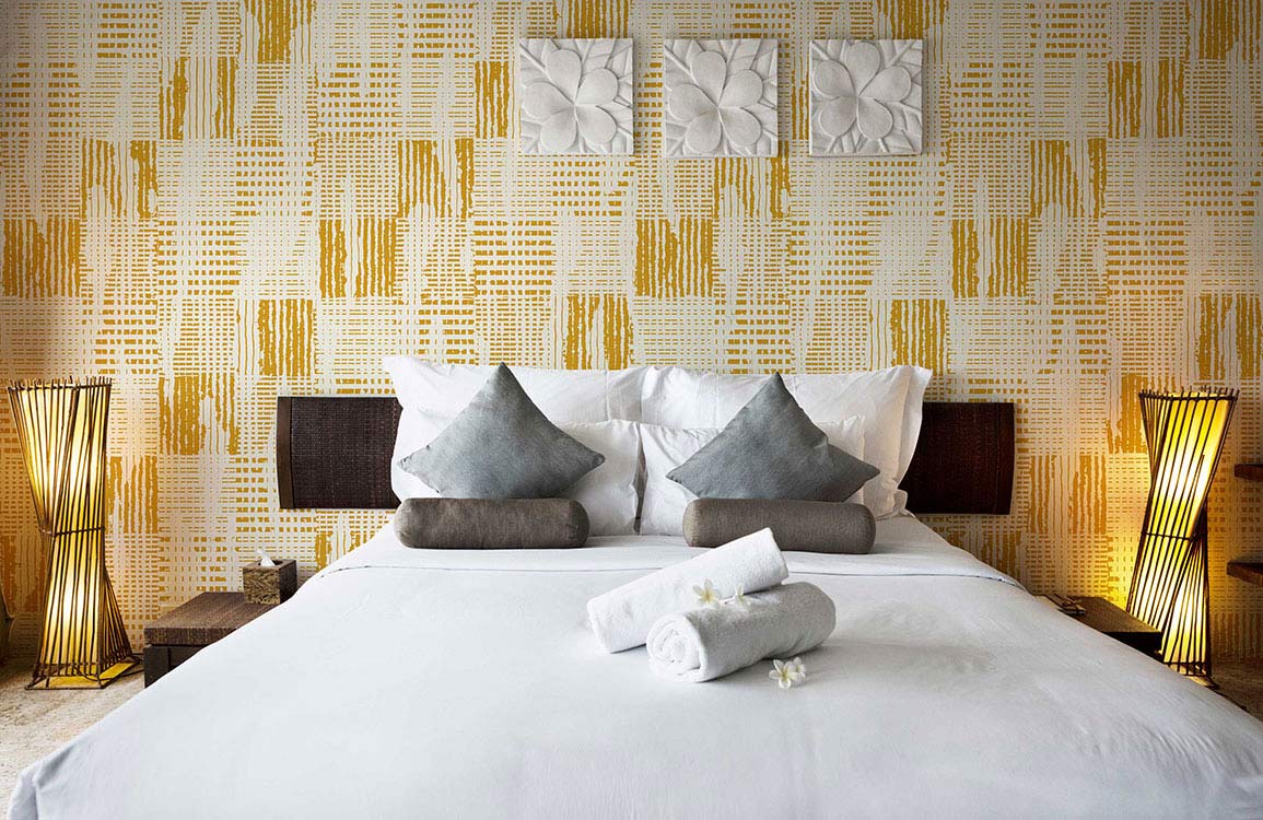 Vintage mustard geometric wallpaper, stylish retro decor, white bed, grey cushions, elegant bedroom setting.