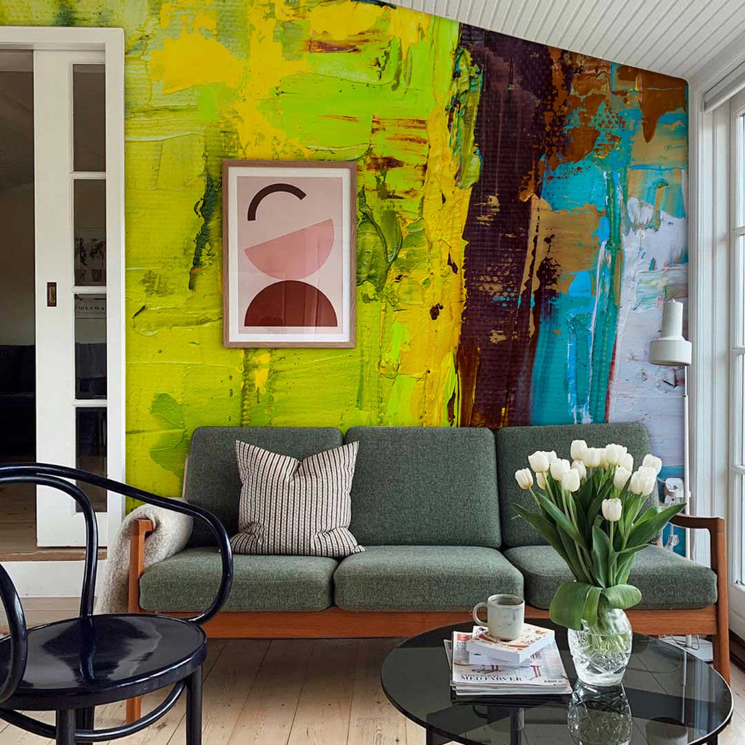 Colourful abstract mural wallpaper in yellow, blue, green tones behind a green sofa in living room.