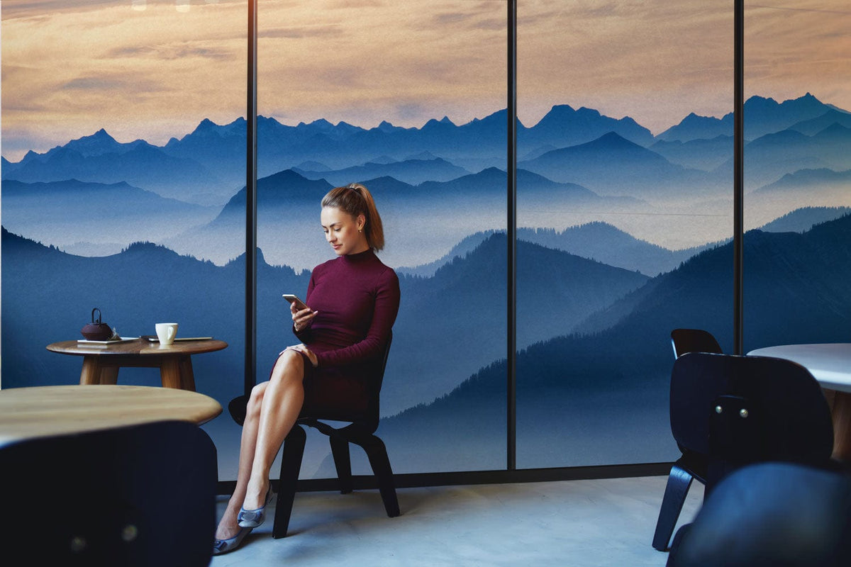 Lady in cafe setting with serene blue mountain mural wallpaper, round wooden tables, and chairs.