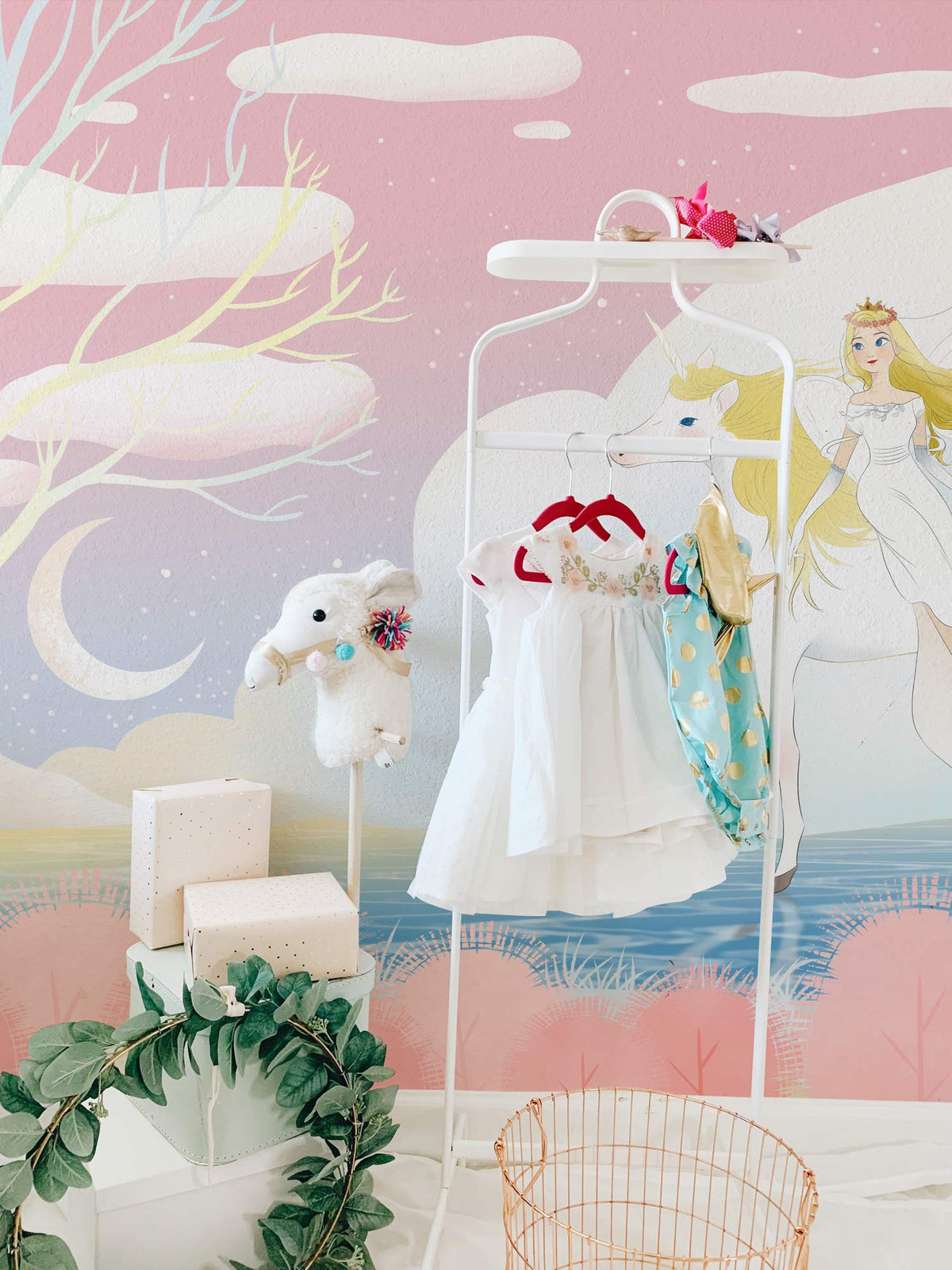 Ethereal unicorn mural wallpaper in pastel pink, with child's dress rack and unicorn plush toy.